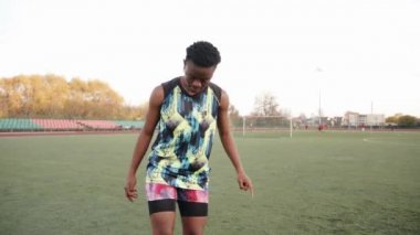 Genç siyahi kız stadyumda antrenman yapıyor ve iki ayağıyla topa hokkabazlık yapıyor. Spor ve aktif yaşam tarzı kavramı