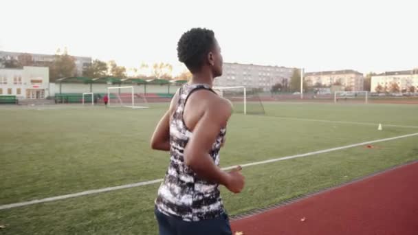 Una joven negra entrenando en el estadio de la ciudad y corre en la cinta de correr alrededor del campo de fútbol. Movimiento lento — Vídeo de stock