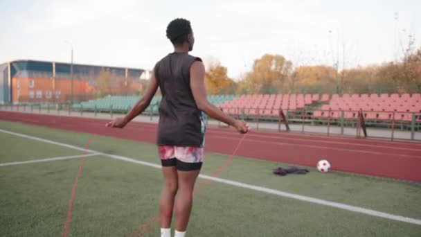 Mladá Afroameričanka trénuje na městském stadionu za slunečného podzimního dne a přeskakuje lano. Zadní pohled. Zpomalený pohyb — Stock video