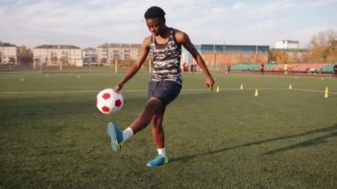 Genç siyahi kız futbol takımı stadyumda antrenman yapıyor ve topu ayaktan ayağa fırlatıyor.
