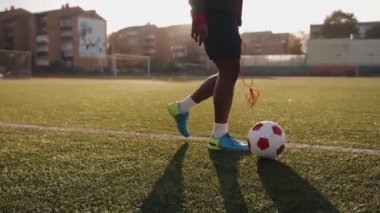 Genç siyah bayan sporcu futbol sahasında antrenman yapıyor ve top sürme tekniğini kullanıyor.
