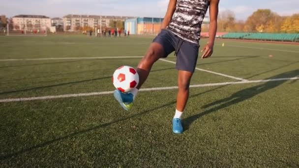 Una joven negra entrenando en un estadio de la ciudad y hace malabares con una pelota de fútbol de un pie a otro. Movimiento lento — Vídeos de Stock