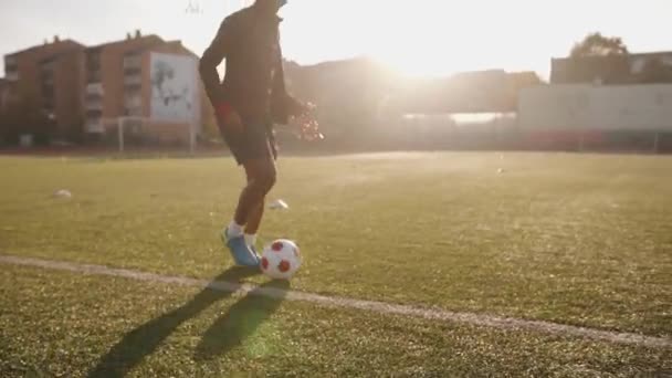 Uma jovem afro-americana atravessa o estádio com uma corda pulando na mão e praticando futebol driblando. Movimento lento — Vídeo de Stock