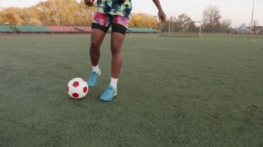 Kolsuz tişörtlü ve şortlu genç Afro-Amerikalı kadın futbol oynuyor ve top oyunları yapıyor.