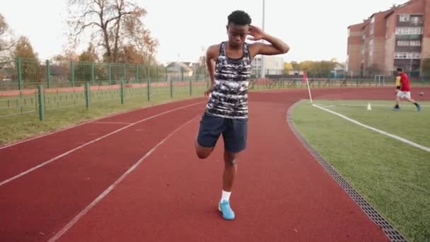Een jong zwart meisje gaat in voor sport op het stadion loopband en doet statische stretching oefeningen. Langzame beweging — Stockvideo