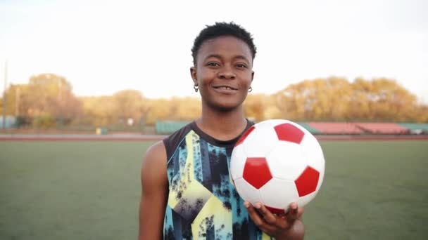 Een jong zwart meisje in een mouwloos T-shirt staat in het stadion tijdens de training en houdt een voetbal in haar hand — Stockvideo