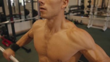 Genç vücut geliştirici spor salonunda çalışıyor halter ütülüyor ve omuz kemerinin kaslarını sallıyor.