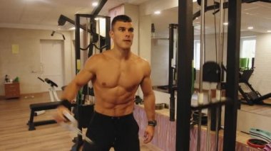 Genç bir adam spor salonunda antrenman yapıyor ve deltoid kaslarını çalıştırmak için çapraz kol kaldırma simülatörü kullanıyor.