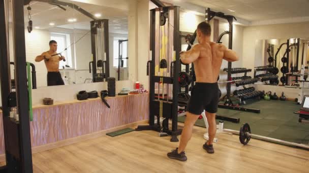 Een bodybuilder in de sportschool en doet een horizontale trek naar de borst op de crossover simulator voor de breedste spieren van de rug en biceps — Stockvideo