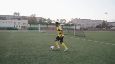 Belarus, Minsk - 20 Haziran 2021: Sarı futbol formalı ve siyah şortlu genç bir kız sahada oynamadan önce top sürme ve hile yapma alıştırması yapıyor.