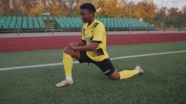Belarus, Minsk - 20 Haziran 2021: Futbol formalı, sahada oynamadan önce ısınan ve bacaklarını esneterek derin hamleler yapan ciddi siyah kız