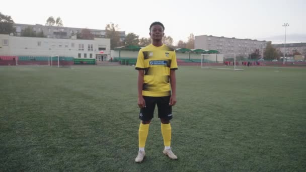 Białoruś, Mińsk - 20 czerwca 2021: Poważna młoda czarna dziewczyna stoi sama na boisku w mundurze piłkarskim i pokazuje zaciśniętą pięść. Zwolnij trochę. Koncepcja określenia — Wideo stockowe