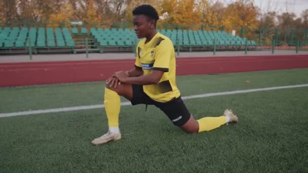 Білорусь, Мінськ - 20 червня 2021 року. Серйозна чорна дівчина у футбольній формі розігрівається перед тим, як грати на полі і робити глибокі сніданки, розтягуючи ноги. — стокове відео