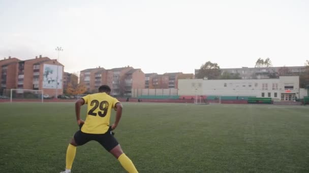 Mladá černoška ve fotbalové uniformě se před zápasem zahřeje na hřišti a zaútočí. Zadní pohled. Zpomalený pohyb — Stock video