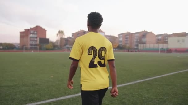 Energetische jonge zwarte man in een voetbal uniform met een nummer op de rug gaat door het stadion en kijkt terug op de camera — Stockvideo