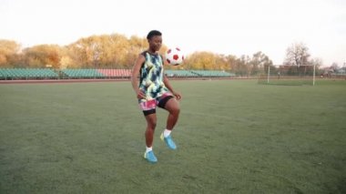 Genç siyahi kız stadyumda antrenman yapıyor ve iki ayağıyla topa hokkabazlık yapıyor. Spor ve aktif yaşam tarzı kavramı