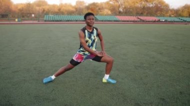 Kendine güvenen, parlak üniformalı genç kız futbol sahasında spor yapıyor ve bacak esnetiyor. Yavaş çekim