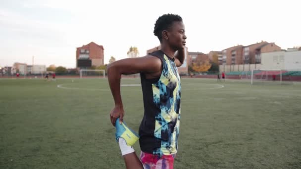 Jong afrikaanse amerikaanse vrouw training op voetbalveld en het doen van statische oefeningen stretching terwijl staan op een been — Stockvideo