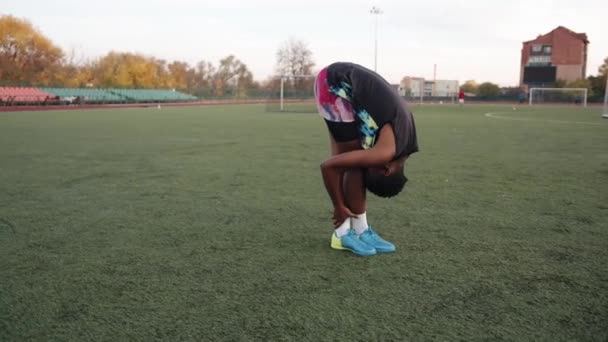 Ung svart flicka tränar på stadens stadion och gör statiska stretching övningar med huvudet tryckt mot knäna — Stockvideo