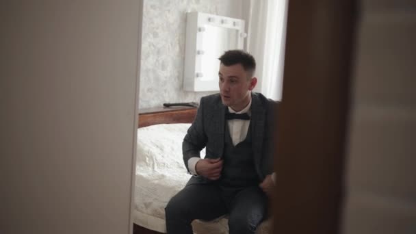 Un hombre joven con un traje gris de tres piezas y una pajarita se mira en el espejo. Miró por la puerta. Concepto de éxito y carrera — Vídeo de stock