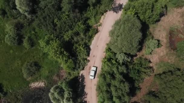 Disparando con un dron de un coche blanco conduciendo a lo largo de una carretera rural rodeada de árboles y arbustos verdes. Concepto de viaje y libertad — Vídeos de Stock