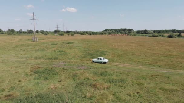 Luchtfoto van een retro auto volga gaz 21 op een versleten baan in een veld in de buurt van een rivier en een elektriciteitsleiding op een zomerdag — Stockvideo