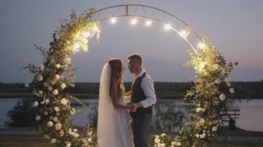 Mutlu yeni evliler havai fişeklerle çevrili bir çiçek kemerinin arka planında dans ediyorlar. Yavaş çekim