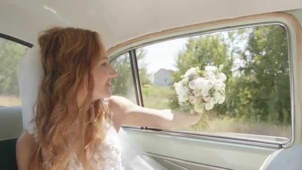 Una giovane sposa affascinante in un velo ha steso la mano con un mazzo da sposa in finestra di un'auto retrò che guida nella natura. Rallentatore — Video Stock