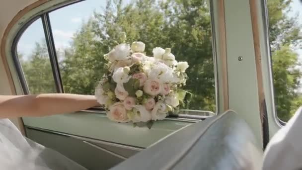 Gelin, doğada yol alan bir arabanın açık camında eli ile muhteşem bir düğün buketi tutuyor. Yavaş çekim — Stok video