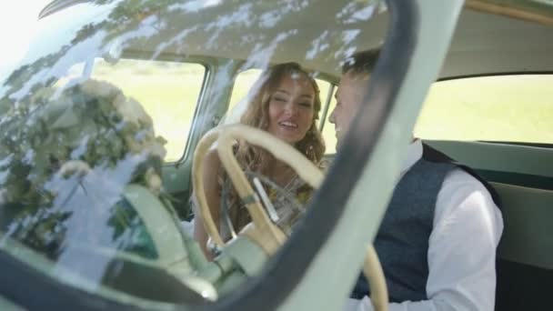 A charming newlywed couple is sitting in the front seat of a retro car and a wedding bouquet on the dashboard. Slow motion — Stock Video