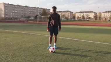 Genç siyahi kız stadyumda antrenman yapıyor ve top taşıma tekniği üzerinde çalışıyor.