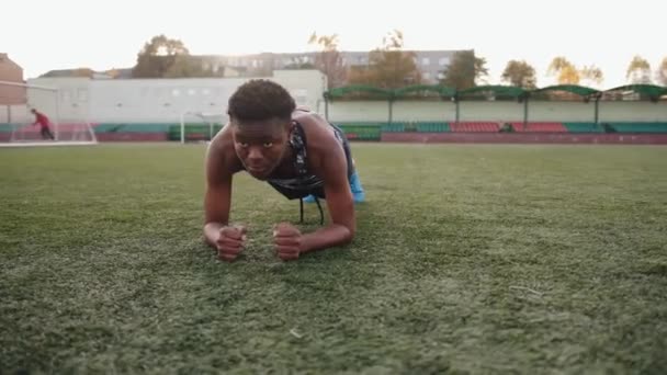 Joven chica negra entrenando en el estadio de la ciudad y empuja hacia arriba en el césped artificial del campo de fútbol — Vídeo de stock