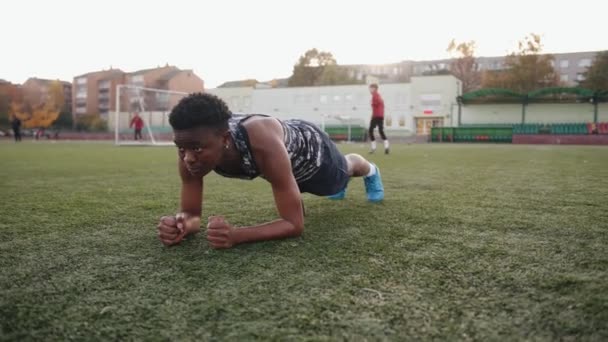 Schattig Afrikaans Amerikaans jong meisje training op voetbalveld in het stadsblok en het doen van oefening plank op een arm — Stockvideo