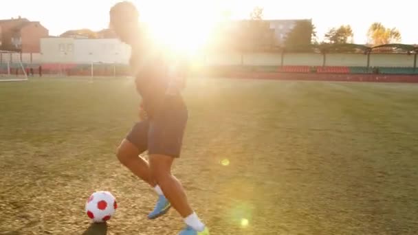 Una mujer afroamericana entrenando en el campo de fútbol y cumple con las fintas con la pelota en movimiento. Movimiento lento — Vídeo de stock