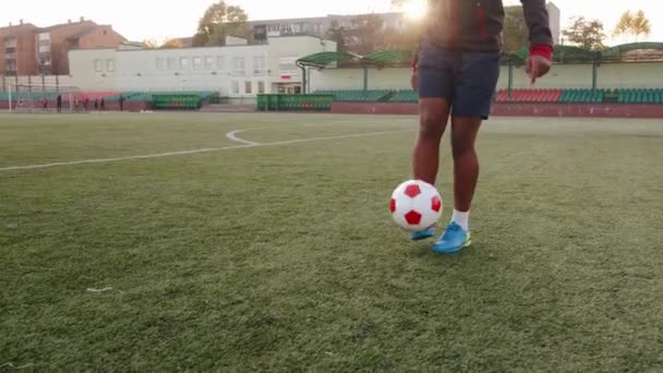 Un jugador de fútbol negro entrenando en un estadio de la ciudad y hace malabares con una pelota en una pierna. Primer plano. Movimiento lento — Vídeos de Stock
