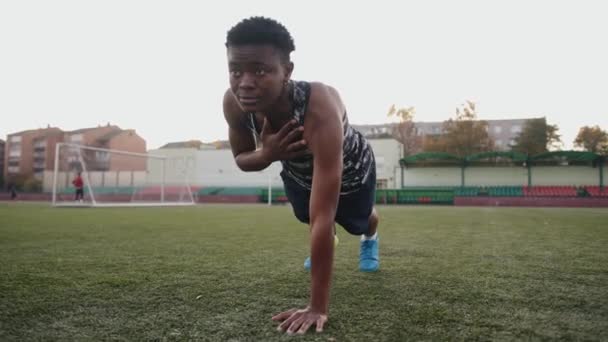 Purposeful young black girl training at the city stadium and standing in a plank on one arm to strengthen the muscles of the whole body — Stock Video