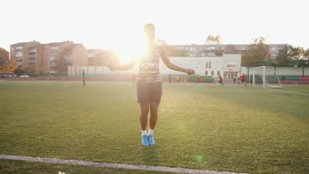 Gadis kulit hitam muda dengan baju tanpa lengan dan celana pendek berlatih di stadion kota dan melompati tali lompat di lapangan sepak bola — Stok Video