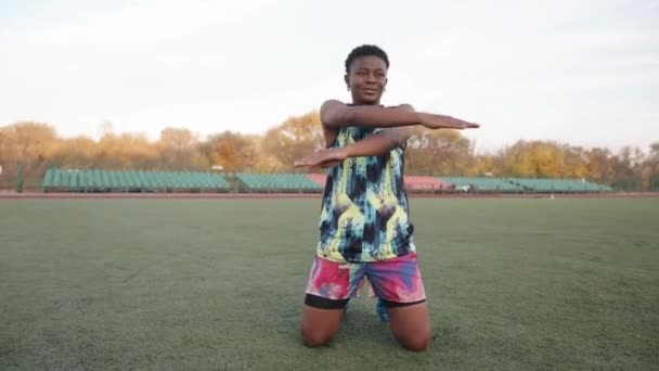 Jovem menina negra trabalhando no estádio da cidade e fazendo exercícios de alongamento estático com a cabeça pressionada de joelhos — Vídeo de Stock