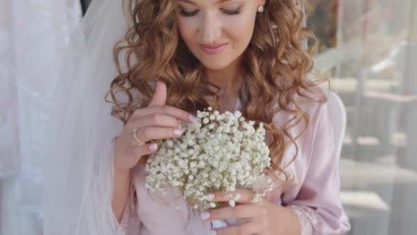 Μια τρυφερή νεαρή νύφη με πέπλο κρατά ένα μπουκέτο γυψόφυλλες στα χέρια της και αγγίζει τα λευκά λουλούδια με το χέρι της. Αργή κίνηση — Αρχείο Βίντεο