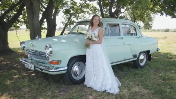 Bielorussia. Regione di Gomel. 21 agosto 2021: Una giovane sposa spettacolare con un bouquet in mano si trova vicino al raro gaz Volga 21 — Video Stock