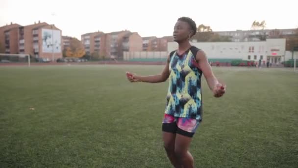 Active young black girl in a bright tracksuit trains on the soccer field and jumping rope. Sport and healthy lifestyle concept — Stockvideo