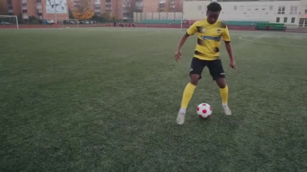 Bielorrusia, Minsk - 20 de junio de 2021: Joven negra con camiseta de fútbol amarilla y pantalones cortos negros practicando driblar antes de jugar en el campo y fingir con la pelota — Vídeos de Stock