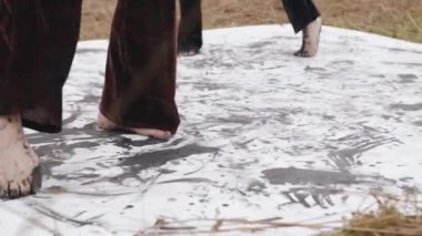 İki genç kız sahada dans ediyor ve ayakları siyah boyayla kaplanmış tuvalde resim yapıyorlar. İkincil performans