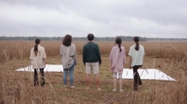 Bir adam ve iki genç kız çıplak ayakla sırayı terk ediyor ve doğadaki bir gösteri için buğday tarlasında platformlarda dikiliyorlar.