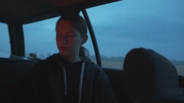 Tatlı genç bir kız camlarında yağmur damlaları ve yüzünde ateş yansıması olan bir arabada oturuyor.