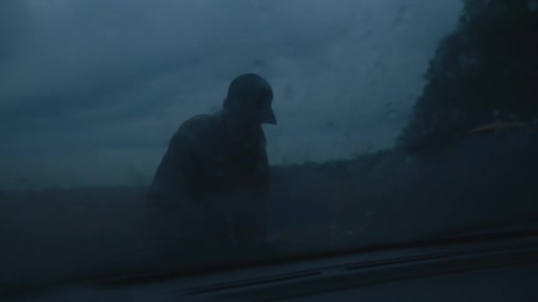 Joven con gorra y una chica cerca de una tienda de campaña en las afueras del bosque a través del parabrisas de un coche en gotas de lluvia — Vídeos de Stock