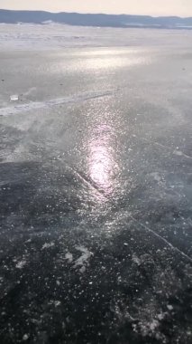 Baykal Gölü 'nün yüzeyinde şeffaf bir buz parçası kırılır ve güneşte küçük parçalara ayrılır. Dikey video. Yavaş çekim