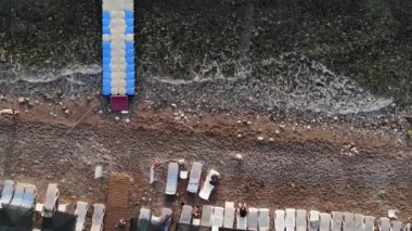Plastik modüler dubaların deniz manzarası ve çakıl taşlı sahildeki tatilcilerle güneş pansiyonları. Uzaklaştırma efekti