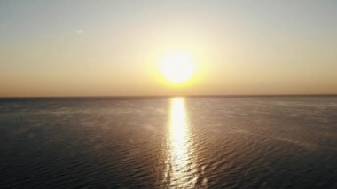 Gün batımında ya da şafakta sakin bir denizin drone atışları ve berrak bir gökyüzüne karşı güneşten gelen su dalgaları içinde parlak bir yol.