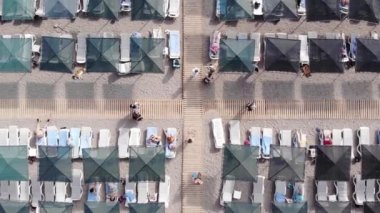 Sahilde şemsiyelerin altında sıralanmış güneş panzelerinin ve yürüyen ve güneşlenen turistlerin en üst görüntüsü. Uzaklaştırma efekti